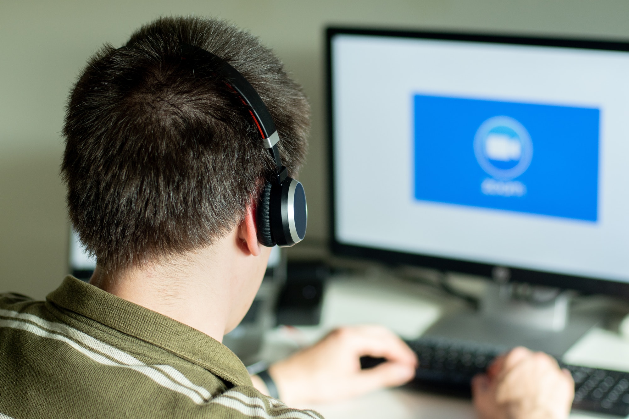 Man with headphones looking on the monitor with zoom cloud meetings logo.