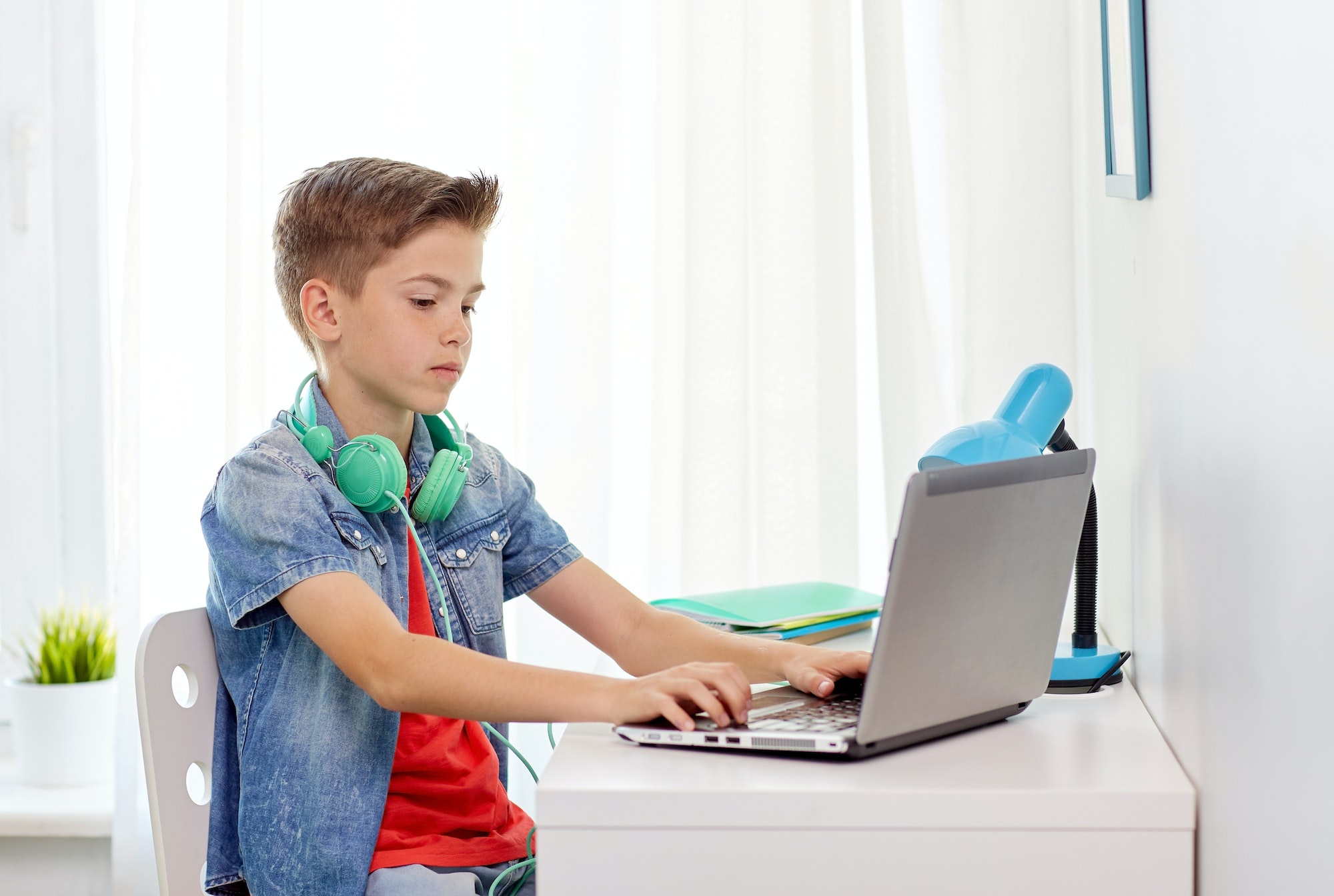 boy with headphones typing on laptop at home