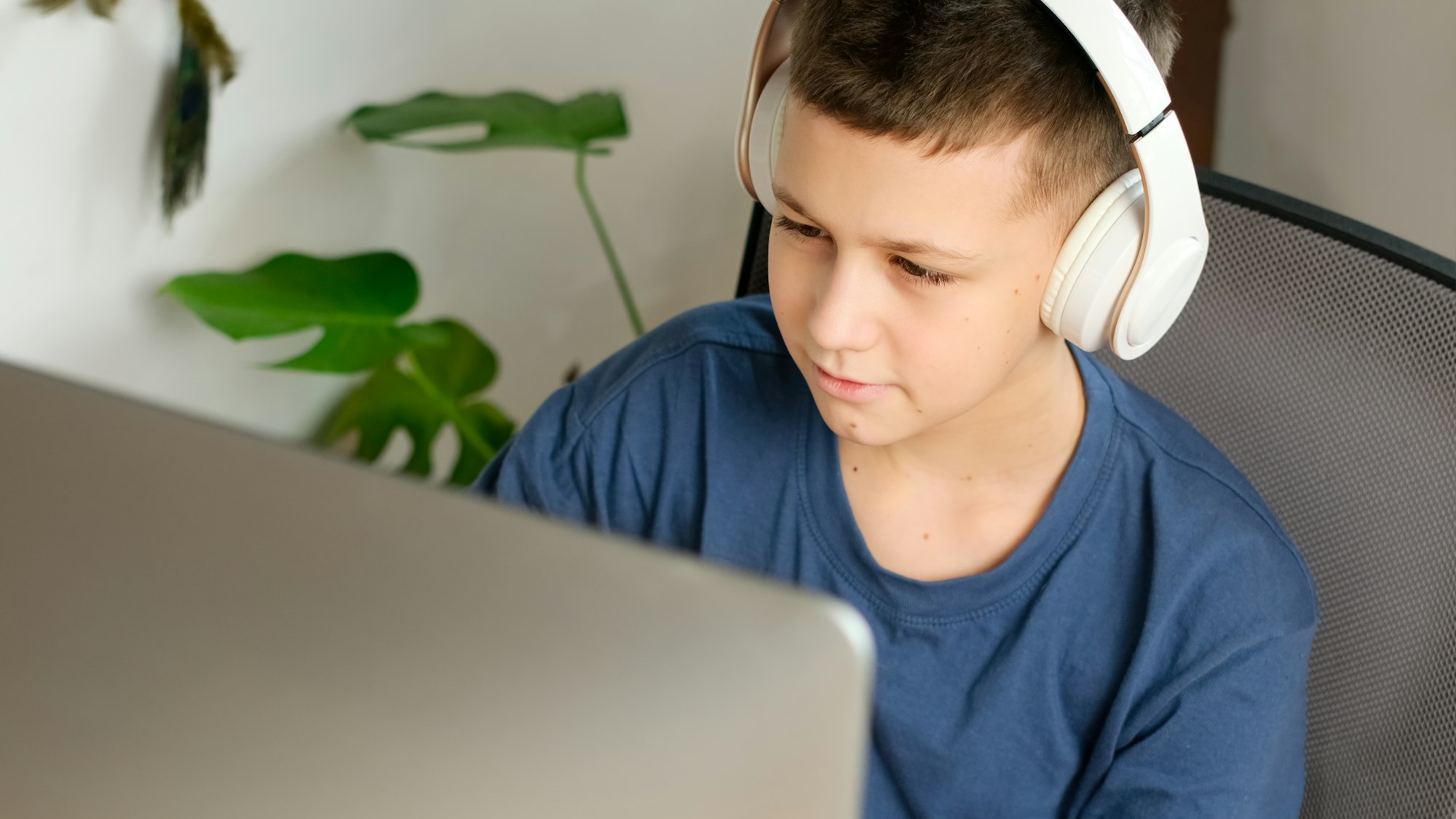 Home learning concept. Teen boy looks at computer monitor wearing headphones.