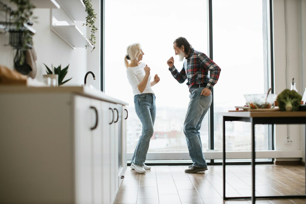 Old couple spends free time dancing twist in modern light kitchen