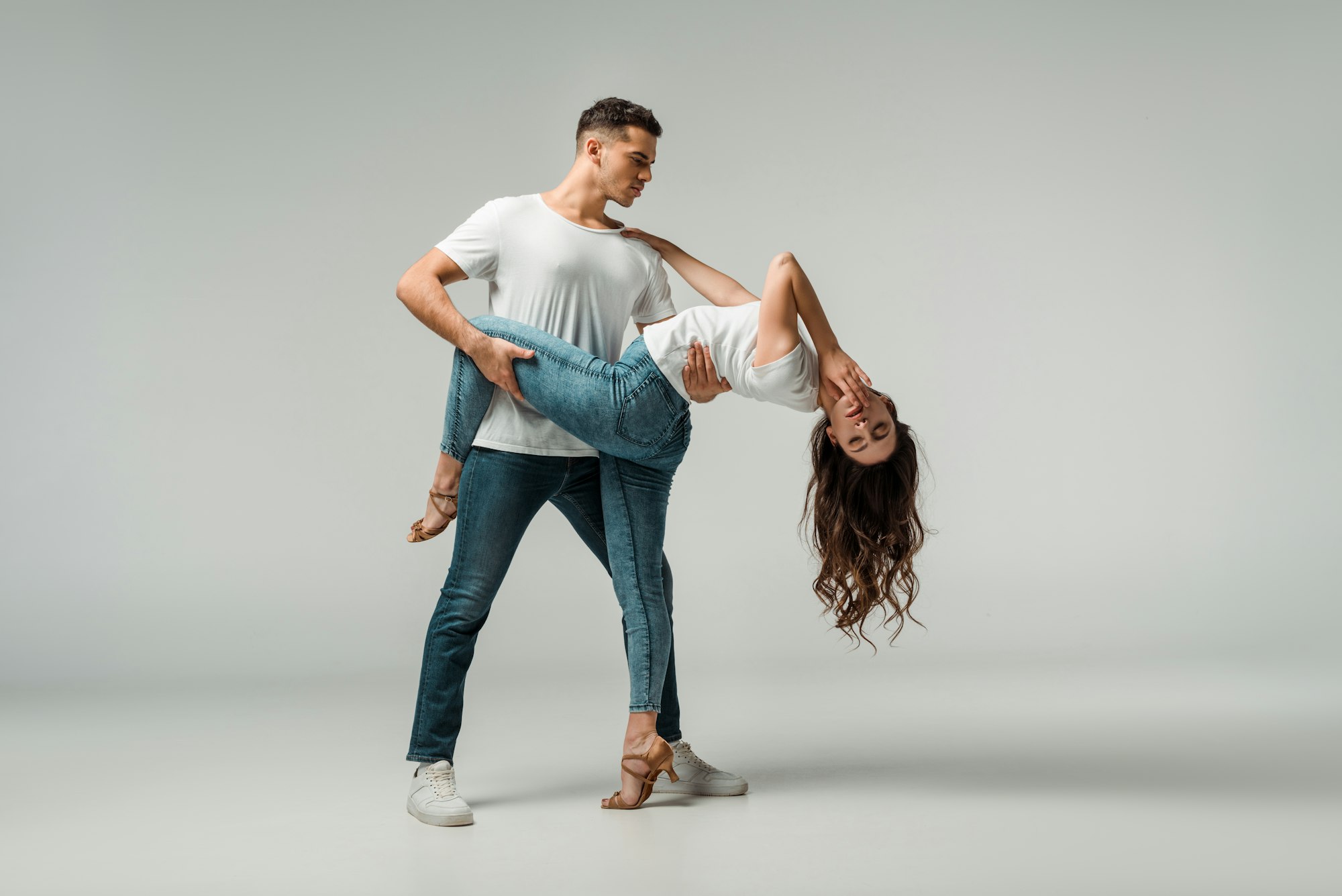 dancers in t-shirts and jeans dancing bachata on grey background